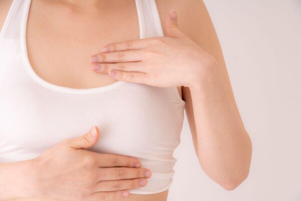 Close up of woman wearing white shirt and massaging left breast with two hands after breast augmentation surgery