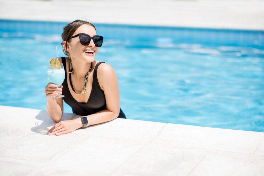 beautiful woman in black swimsuit relaxing with cocktail at the swimming pool outdoors