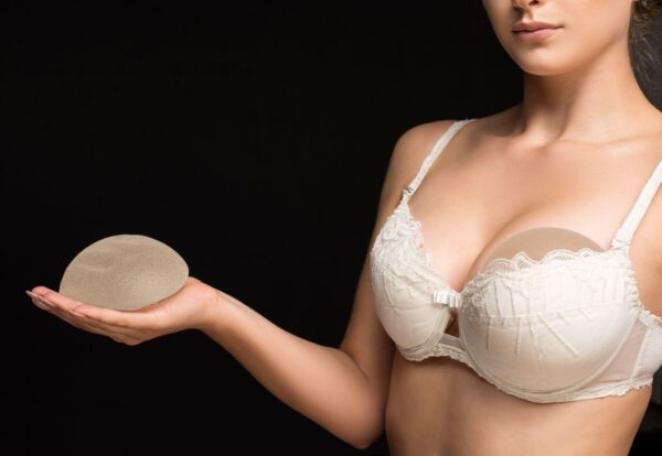 woman holding breast implant with one hand and the other implant in the bra she is wearing