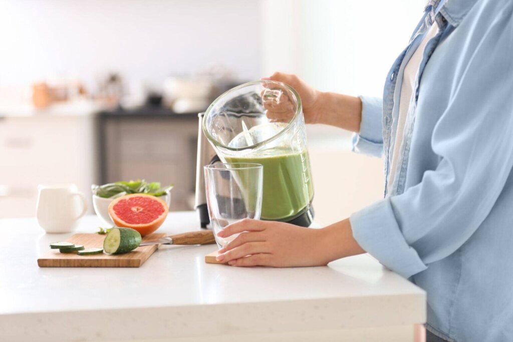 woman pouring tasty smoothie from blender into glass in kitchen