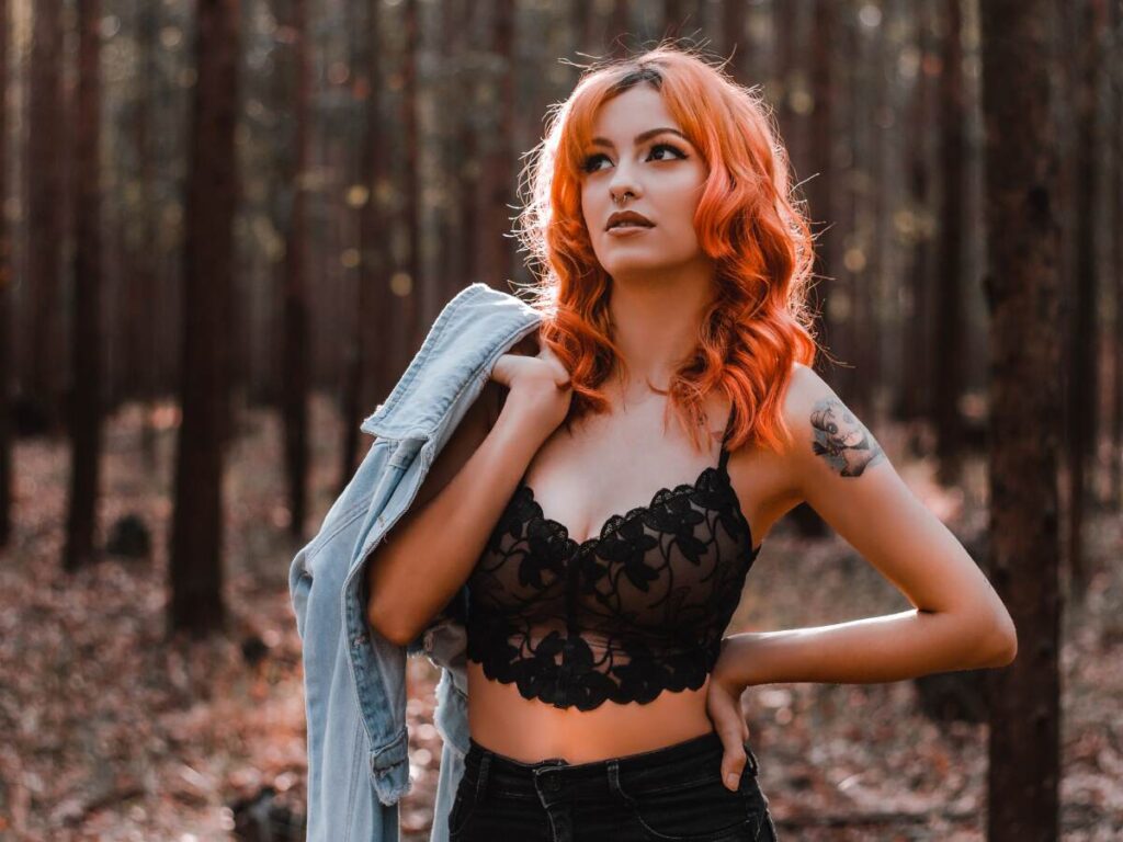 woman with red hair standing outside in small black lace shirt holding denim jacket