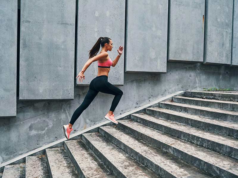 young woman in sports clothing jogging while exercising on the steps outdoors